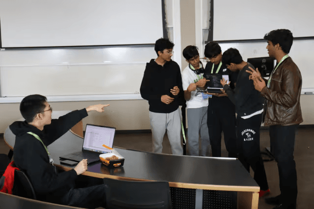 A hackathon team huddled around a laptop in a classroom
